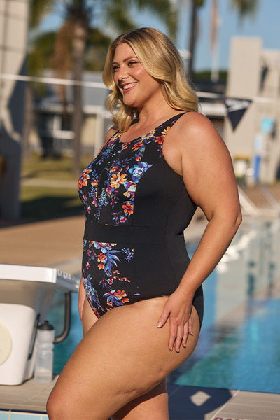 Side of blonde model wearing plus size flattering one piece with zip front detail in blue and orange floral print