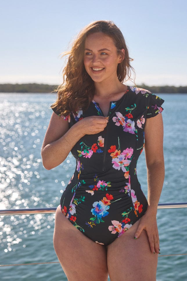 Model wearing black floral frill sleeve zip front swimsuit