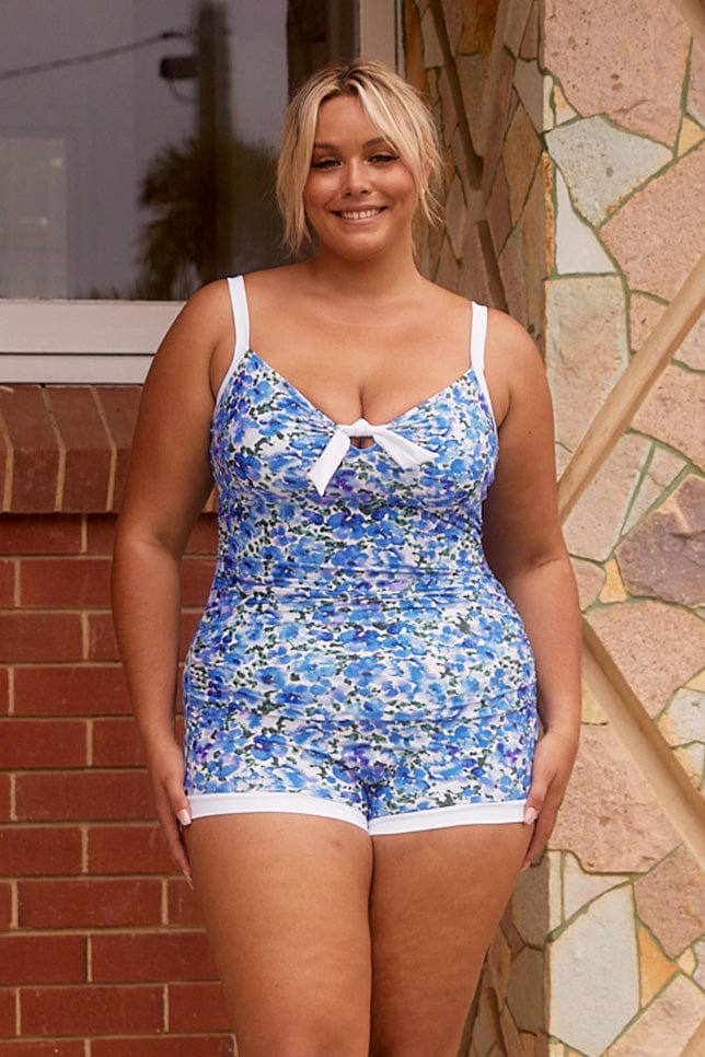 Blonde model wearing plus size boy leg one piece with tie detail in blue and white floral print