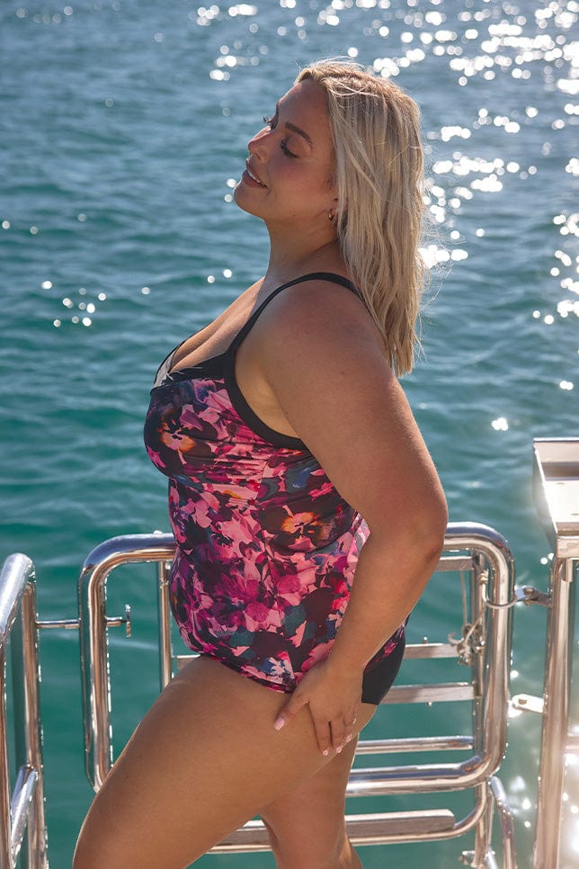 Side of model wearing plus size pink tankini top with black trim