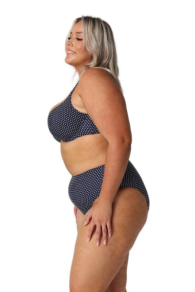 Side profile of model in studio wearing high rise bikini bottoms in navy and white spots for plus size women