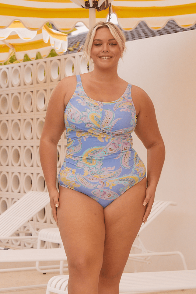 Blonde model wearing a paisley blue and yellow one piece next to pool for curve women