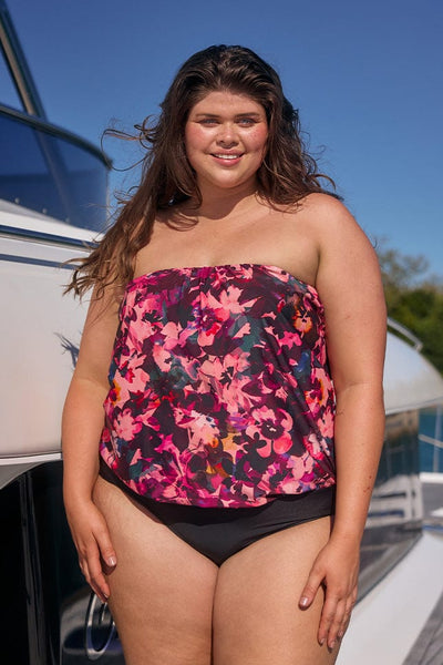 Brunette model on boat wearing plus size flouncy bandeau one piece in pink floral print