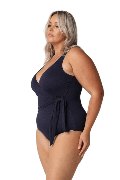 Blonde model in studio wearing wrap tie one piece in navy textured fabric
