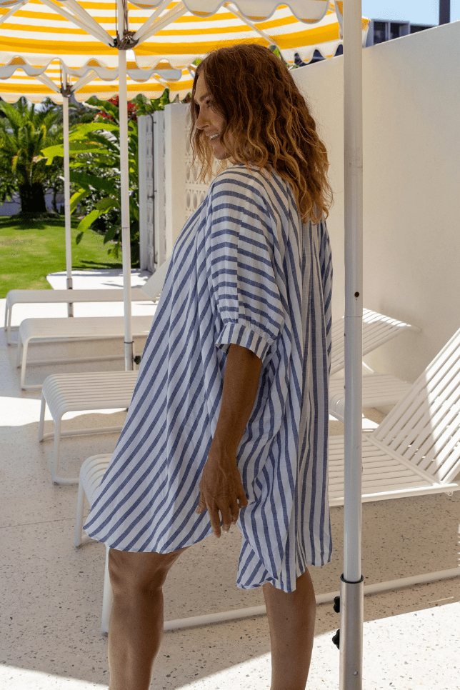 Side profile of model by pool wearing loose fitted navy and blue striped shirt for plus size women