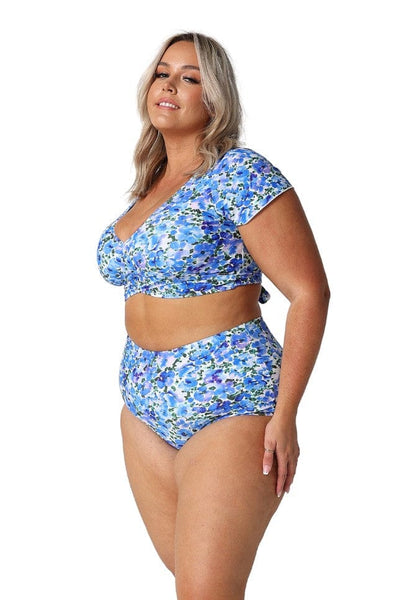 Side profile of blonde curve model wearing blue and white wrap crop bikini top with cap sleeves