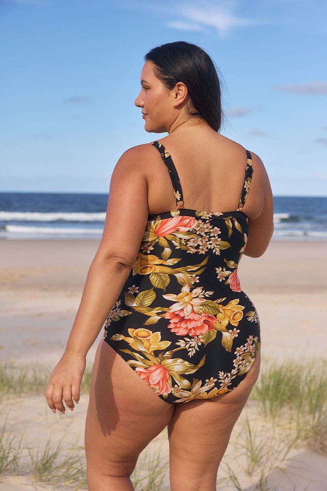 model showing back of black and golf swimsuit at beach