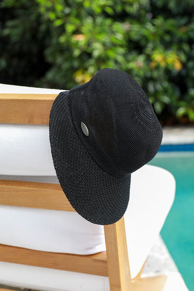 black straw travel hat hanging on a white beach chair by the pool